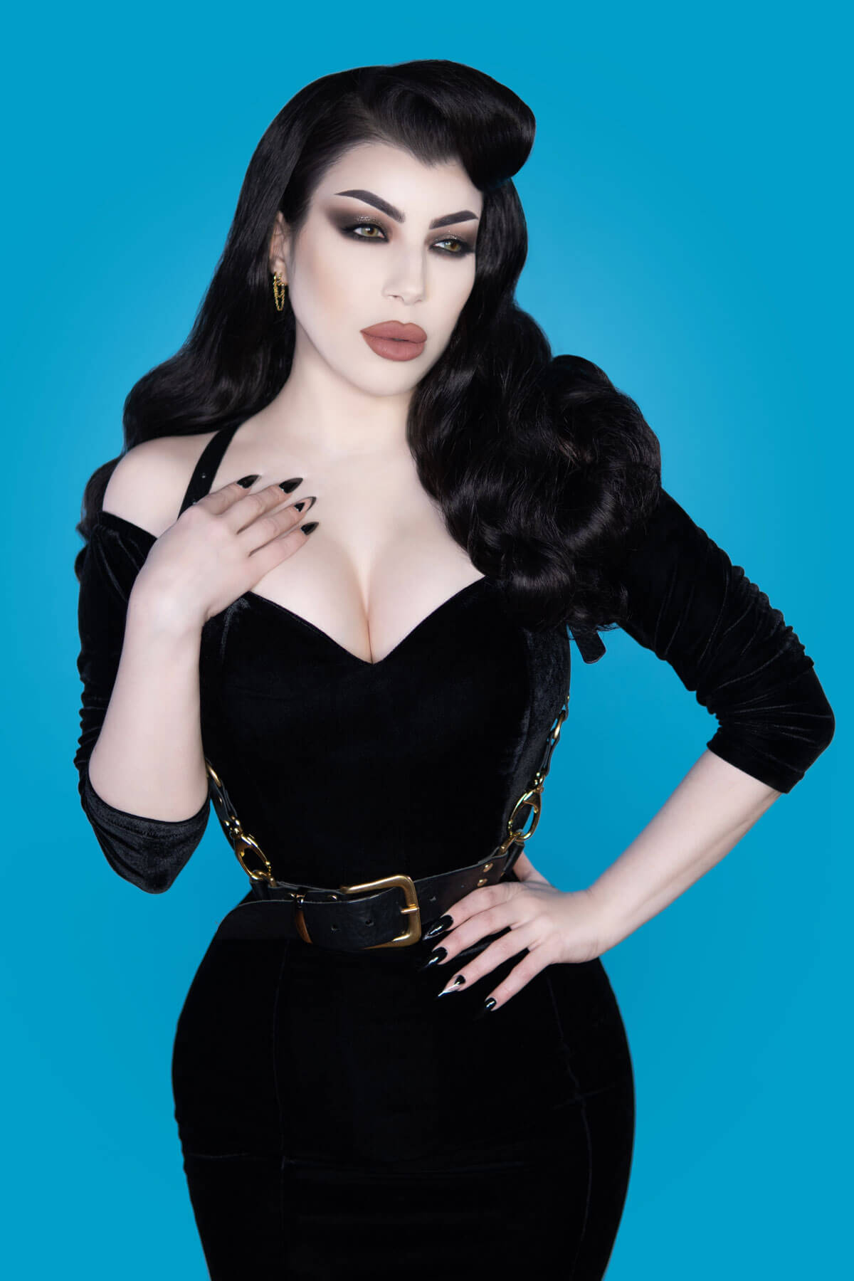 Woman in a black outfit with a gold belt against a blue background. 1950s style half wig hairpiece with beautiful waves: Morgana copper red 130