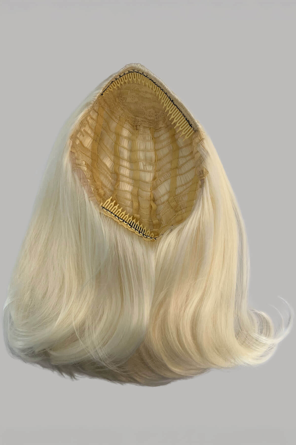 Blonde hair extension with a gold clip on a gray background. 1960s half wig hairpiece, flicked, hair flip: Philippa Platinum blonde 1001