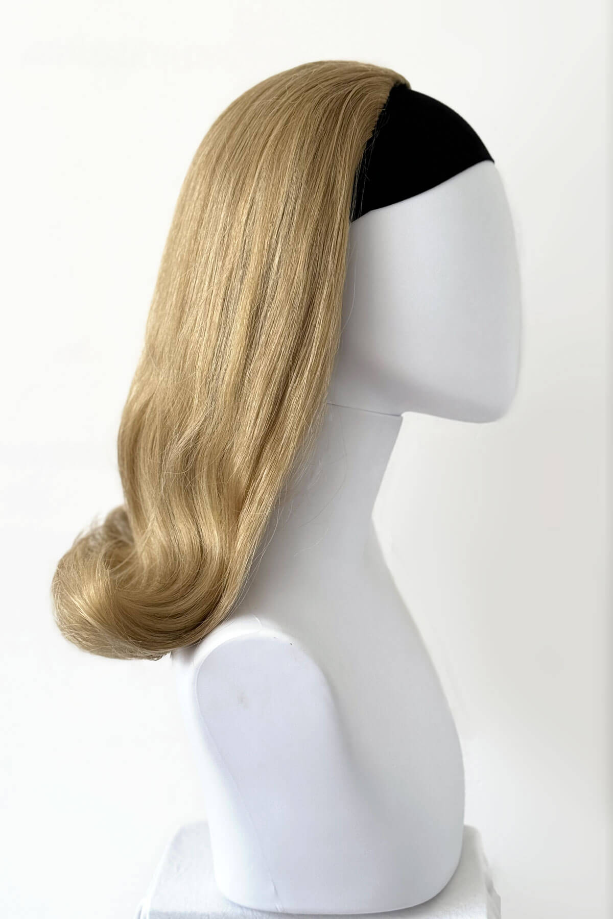Blonde wig on a mannequin head against a white background. 1960s half wig hairpiece, flicked, hair flip: Philippa blonde 24H613