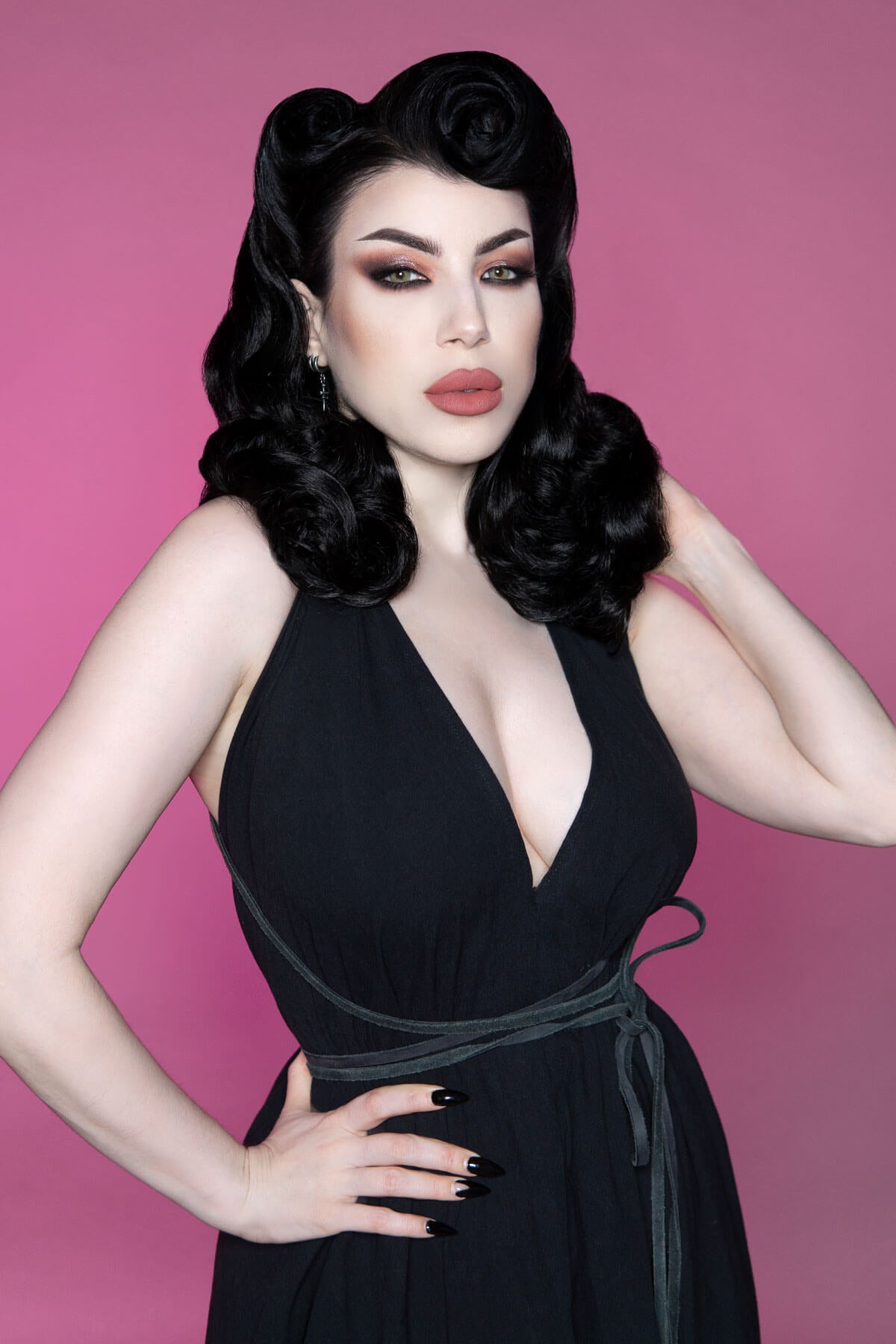 Woman in a black dress with beautiful hair with a pink background. 1950s style shoulder length half wig hairpiece with beautiful vintage waves: Onyx colour jet black 1