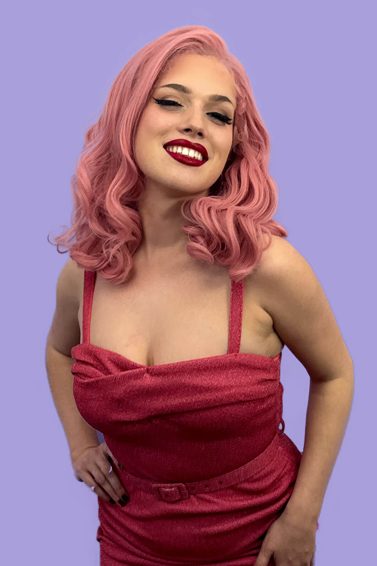 Woman with pink hair and red lipstick wearing a red dress against a purple background. Pink pinup wig, lace front, vintage style: Catalina