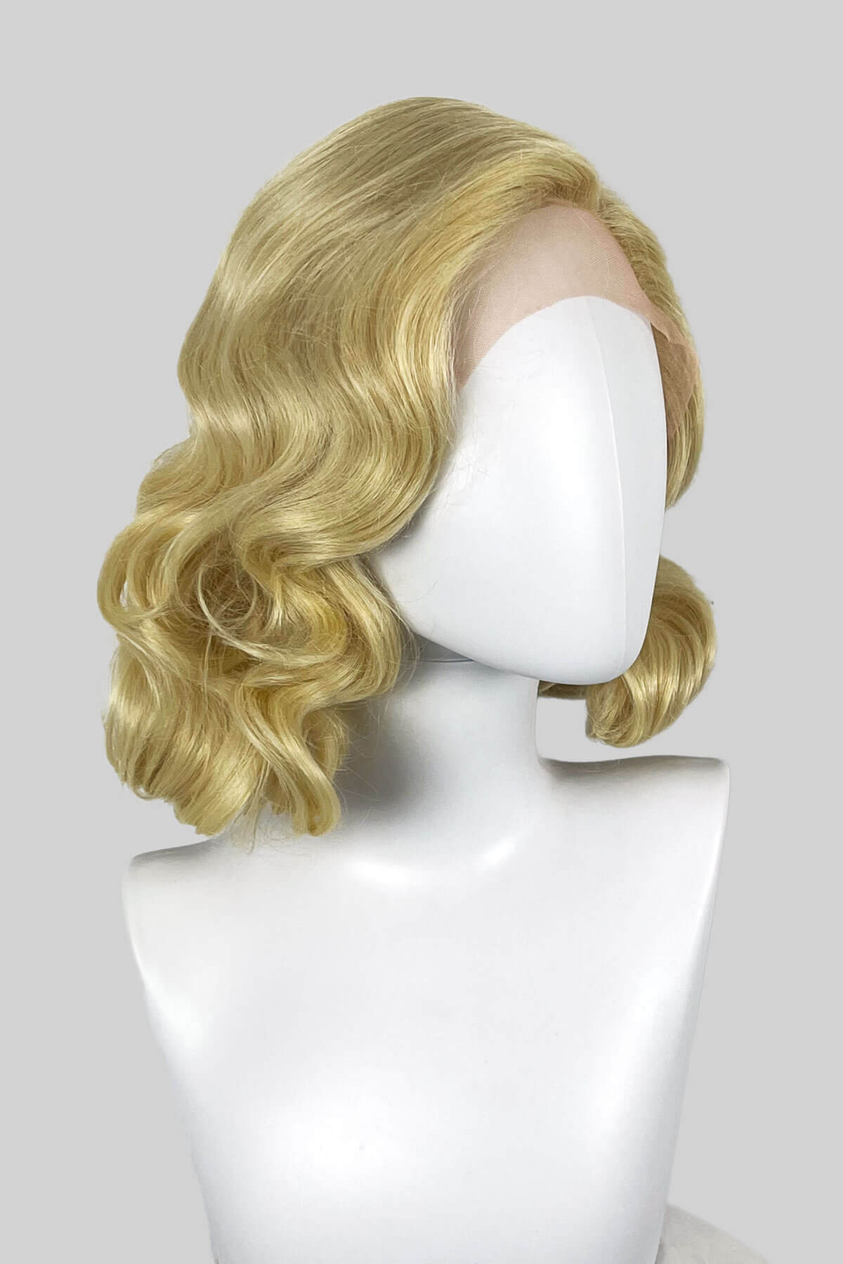 Blonde wig on a mannequin head against a white background. Blonde lacefront wig, pinup/vintage style, mid length with finger waves: Della creamy blonde 613
