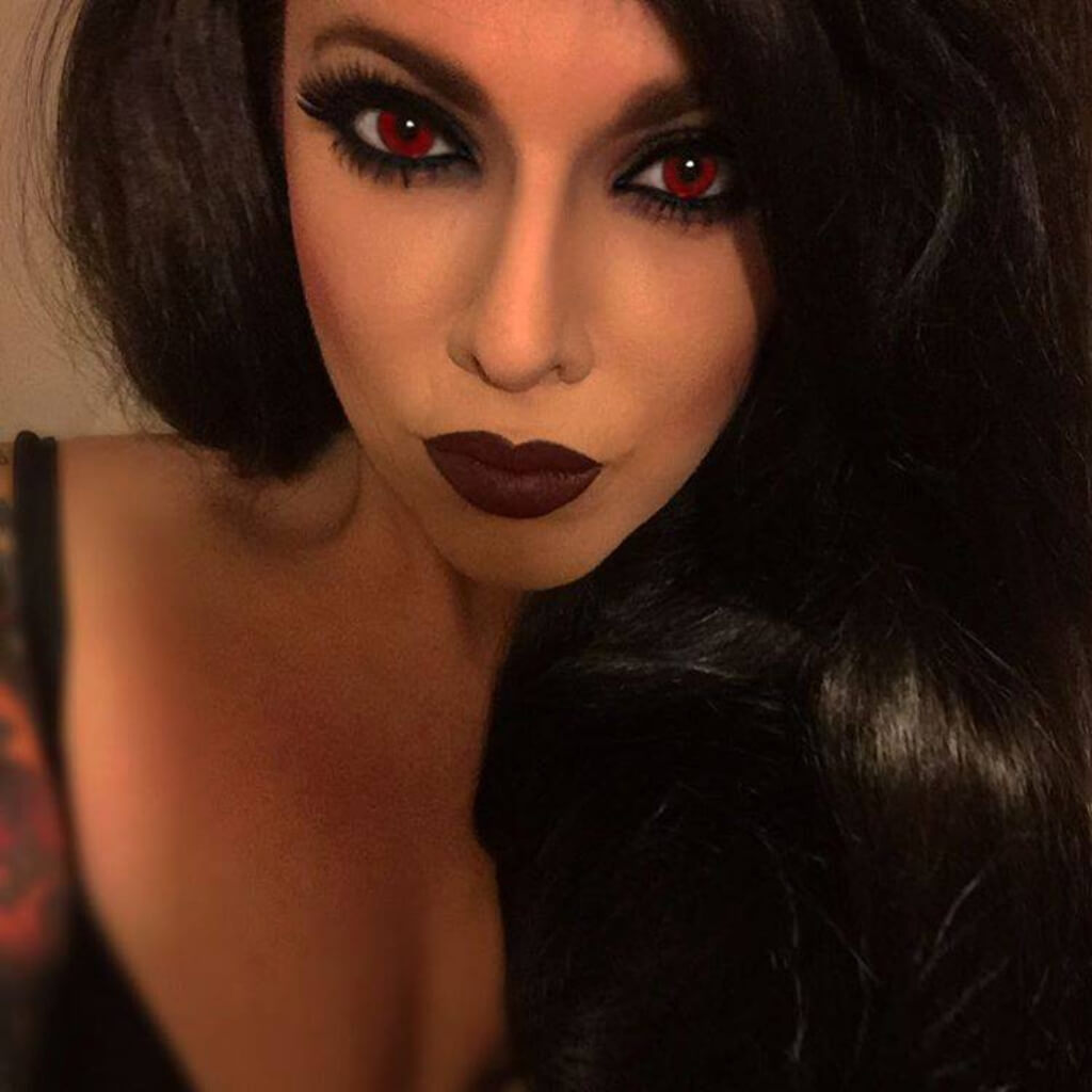 Close-up of a person with dark hair and red eyes, wearing a black top. Long wavy black wig with side-sweeping Fringe: Charlotte