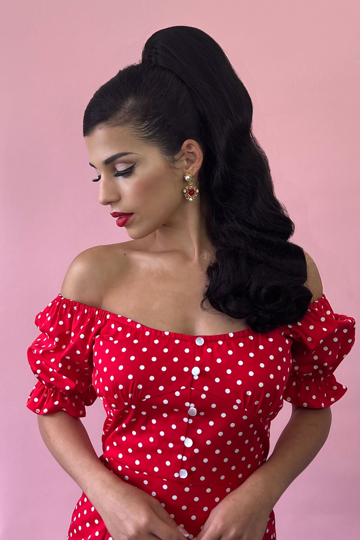 Woman wearing a red polka dot dress with puffed sleeves against a pink background wearing a retro style ponytail hairpiece, long with vintage waves: Arabella black 1B