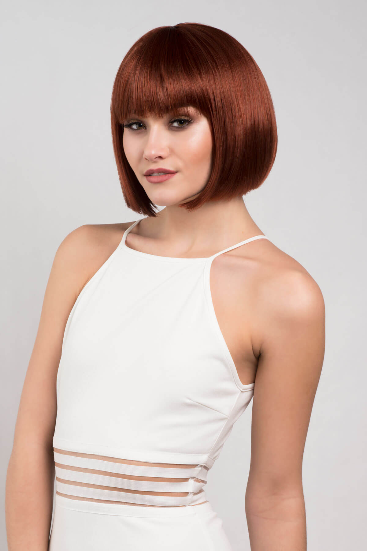 Woman with a stylish bob haircut wearing a white dress against a plain background.Short copper-red/ginger bob wig: Minnie