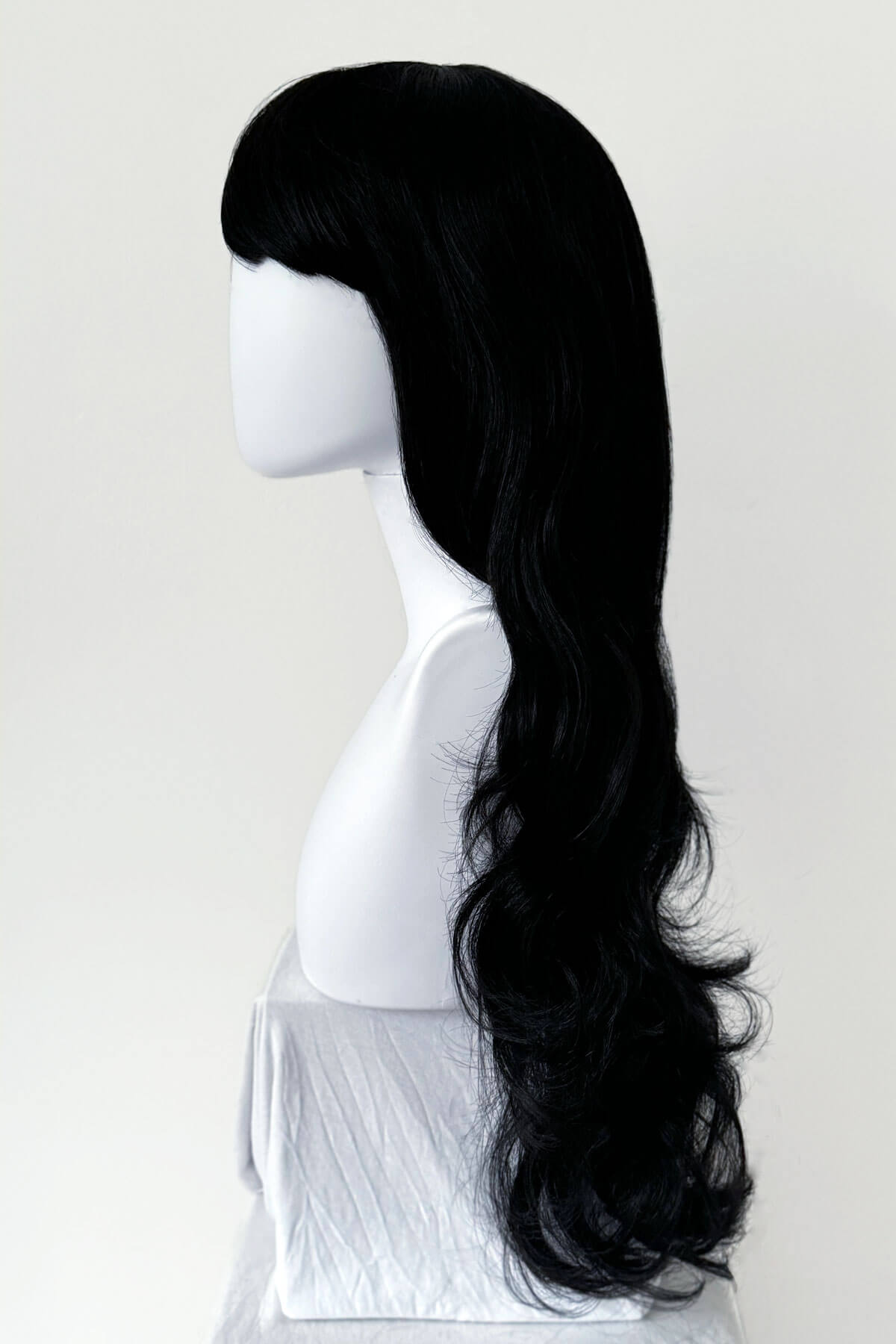 Black wig on a mannequin head against a white background. Long wavy black wig with vintage-style, rockabilly, straight fringe: Eloise
