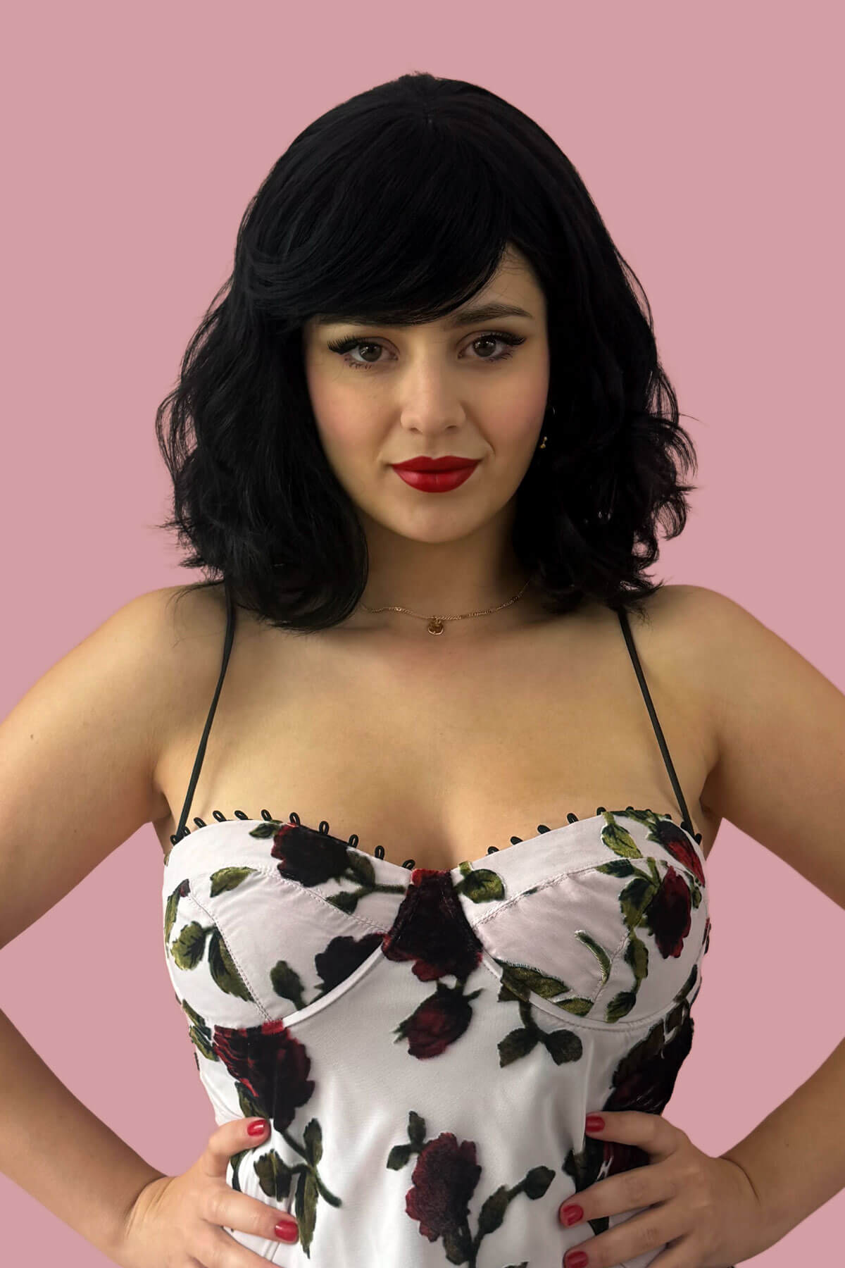 Woman wearing a floral dress with a pink background. Black long wavy bob (lob) wig with swept fringe: Eleena