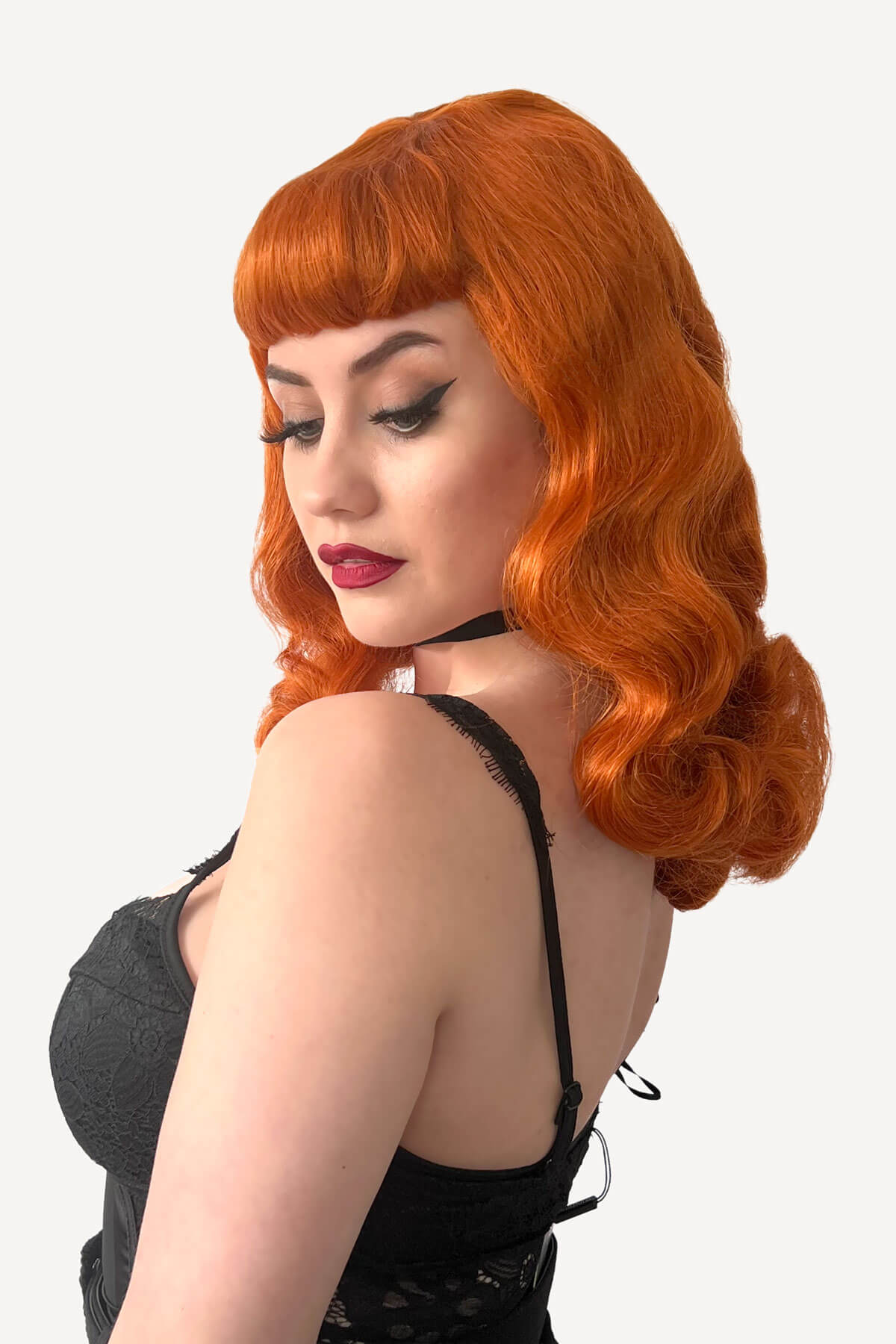 Woman with red hair styled in vintage fashion against a white background. Ginger pinup style wig, finger waved with short fringe, 1950s style: Sienna