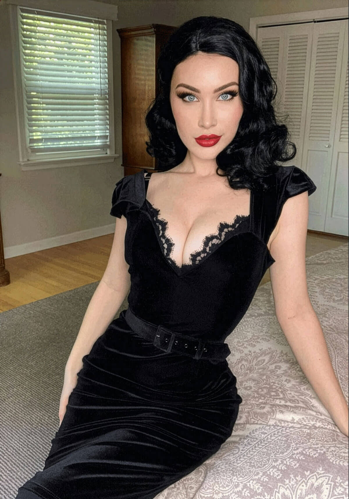 Woman in a black dress sitting on a bed in a room. Black 40s style wig with beautiful marcel waves: Dita