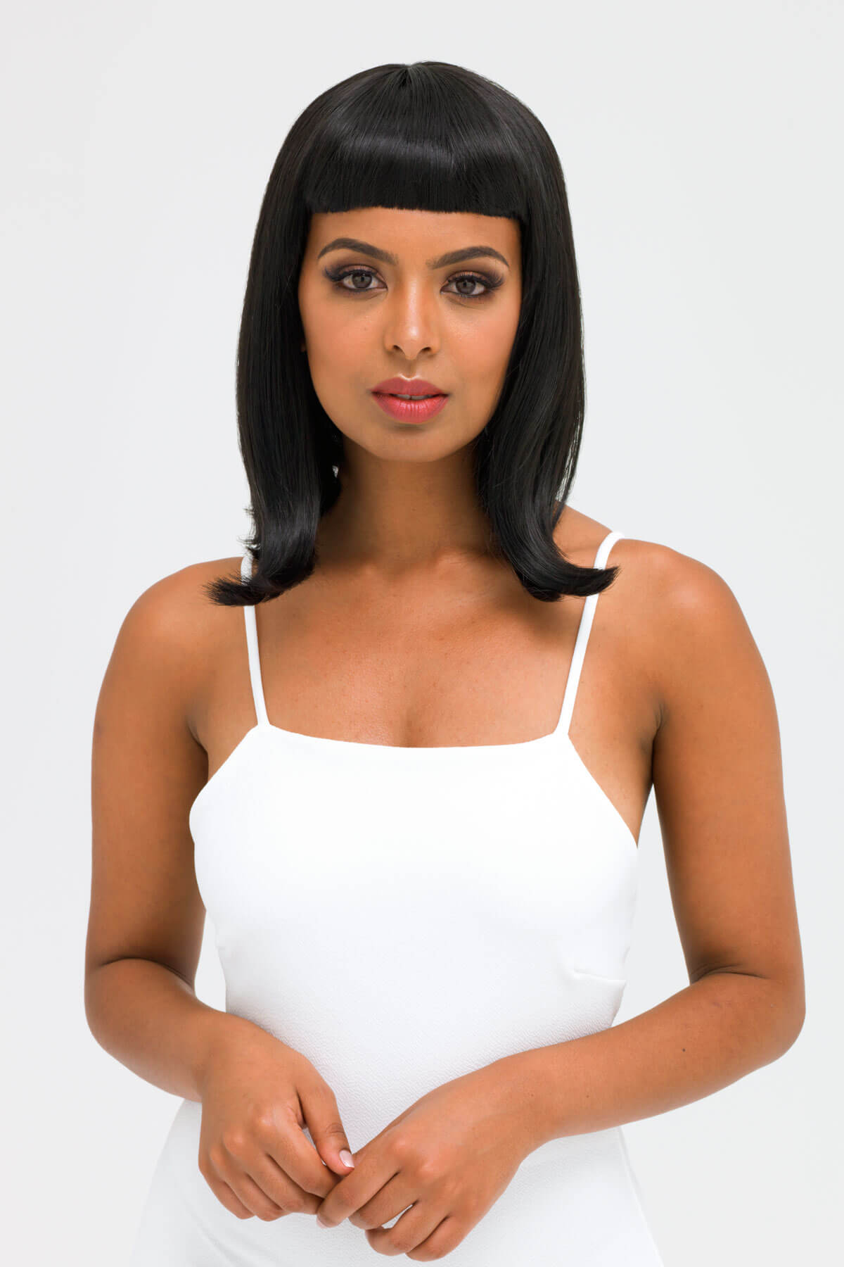 Woman wearing a white tank top with a plain background. Black long bob wig with a short retro, rockabilly-style fringe: Beth