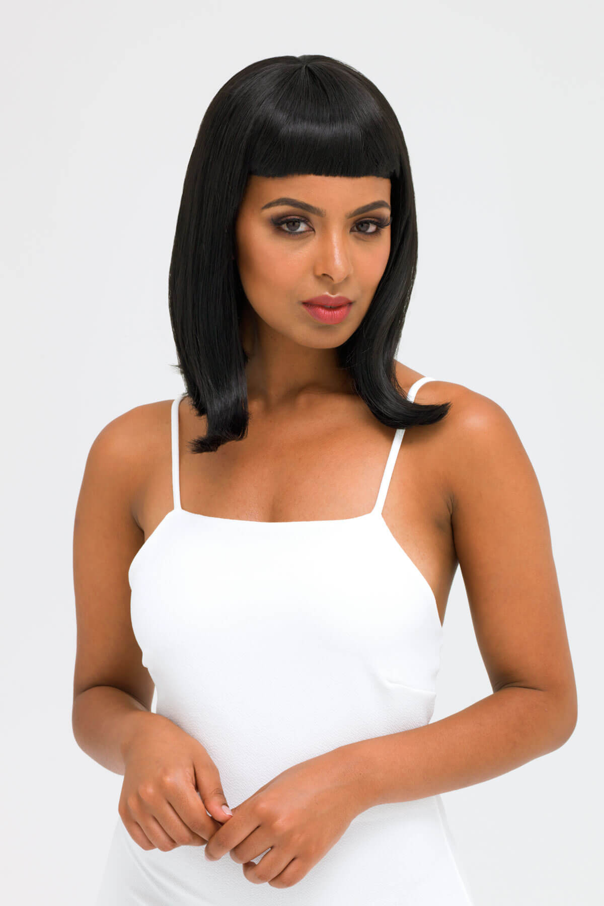Woman wearing a white dress with a plain background. Black long bob wig with a short retro, rockabilly-style fringe: Beth