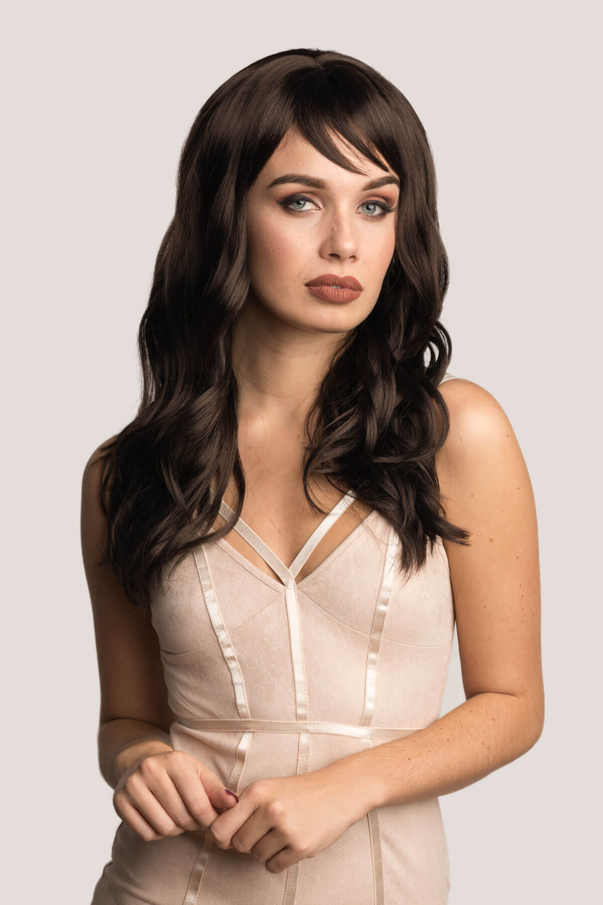 Woman wearing a beige dress with a plain background. Long brown wig with gentle waves: Emma