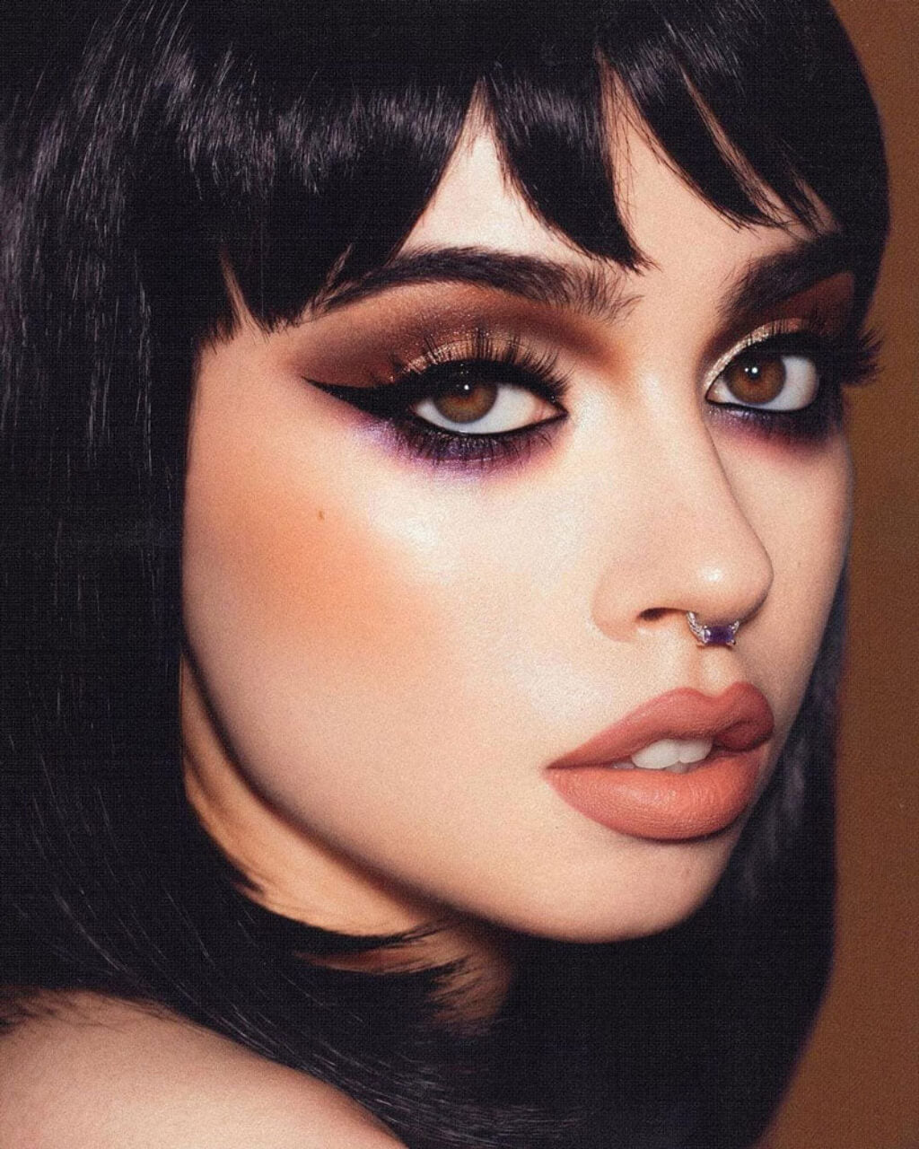 Close-up of a person with dramatic makeup and black hair against a brown background. Black long bob wig, shoulder length: Evie