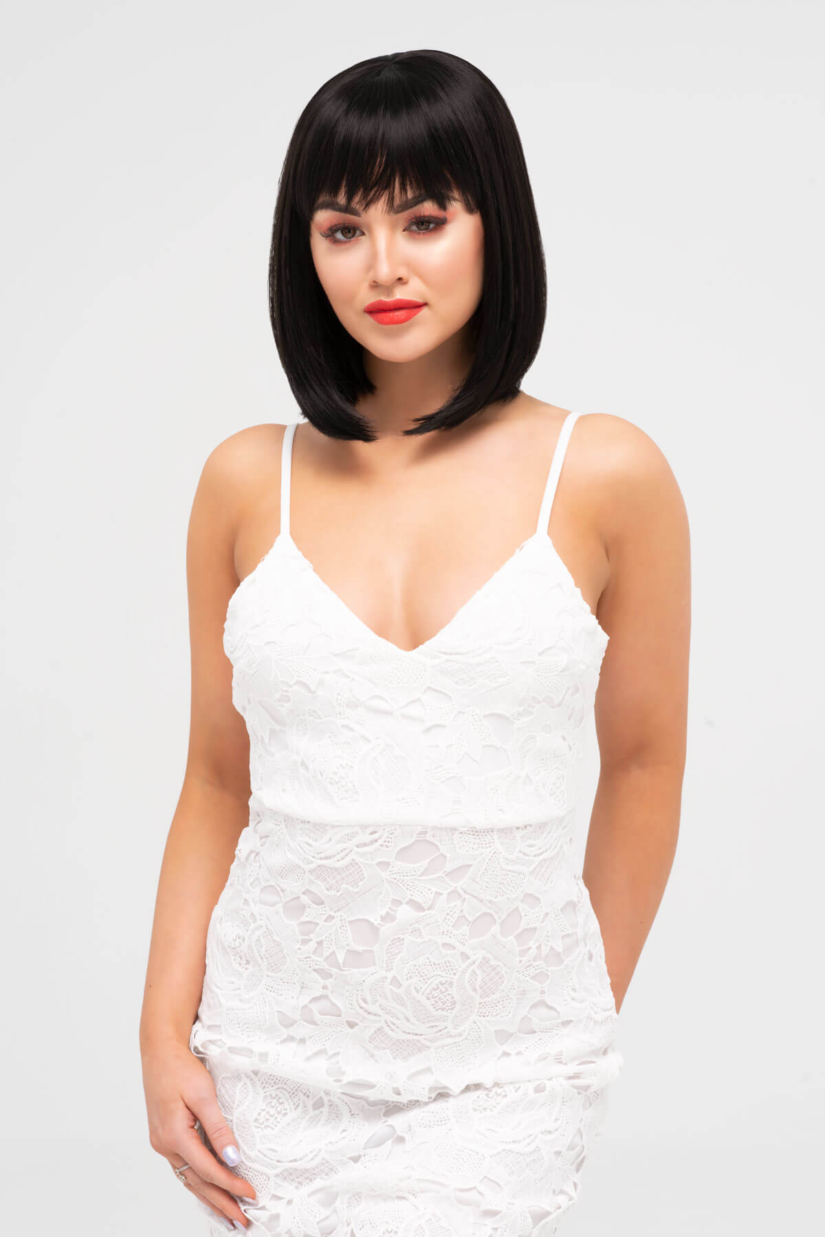 Woman wearing a white lace dress with a plain background. Black long bob wig, shoulder length: Evie