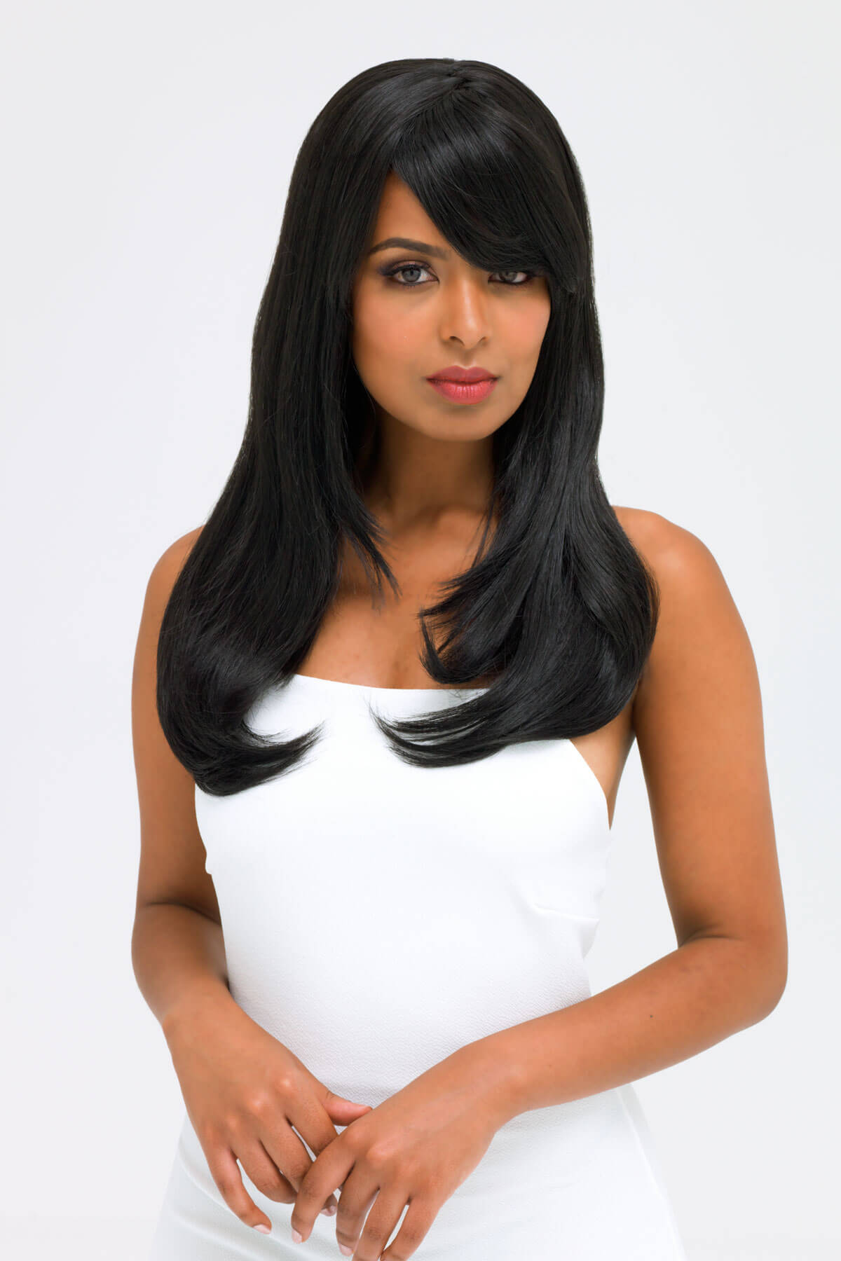Woman with long black hair wearing a white dress on a light gray background. Long black wig, face frame style with full, sweeping fringe: Corina