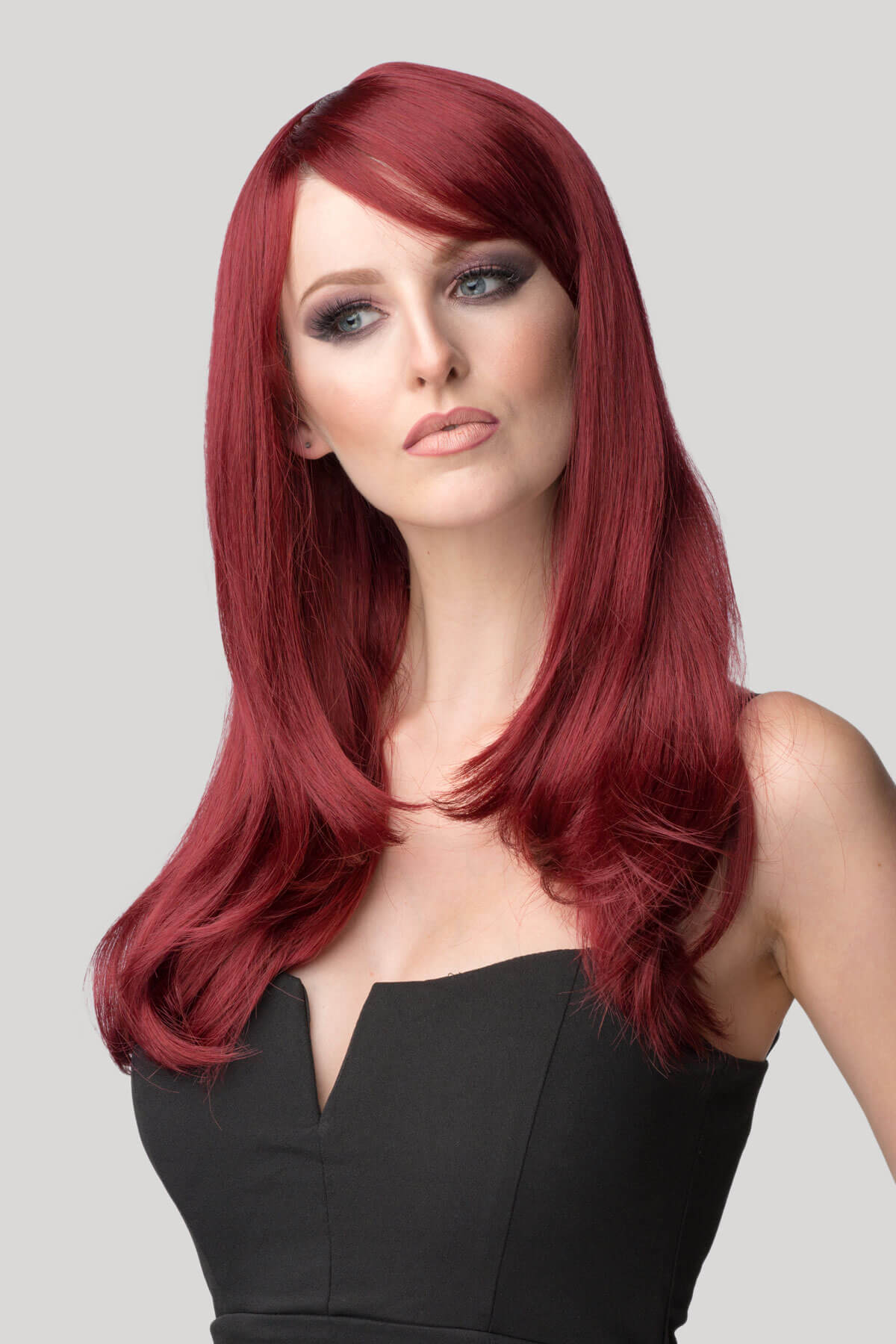 Woman with long red hair wearing a black top on a gray background. Long red wig in razor cut, face frame style: Megan
