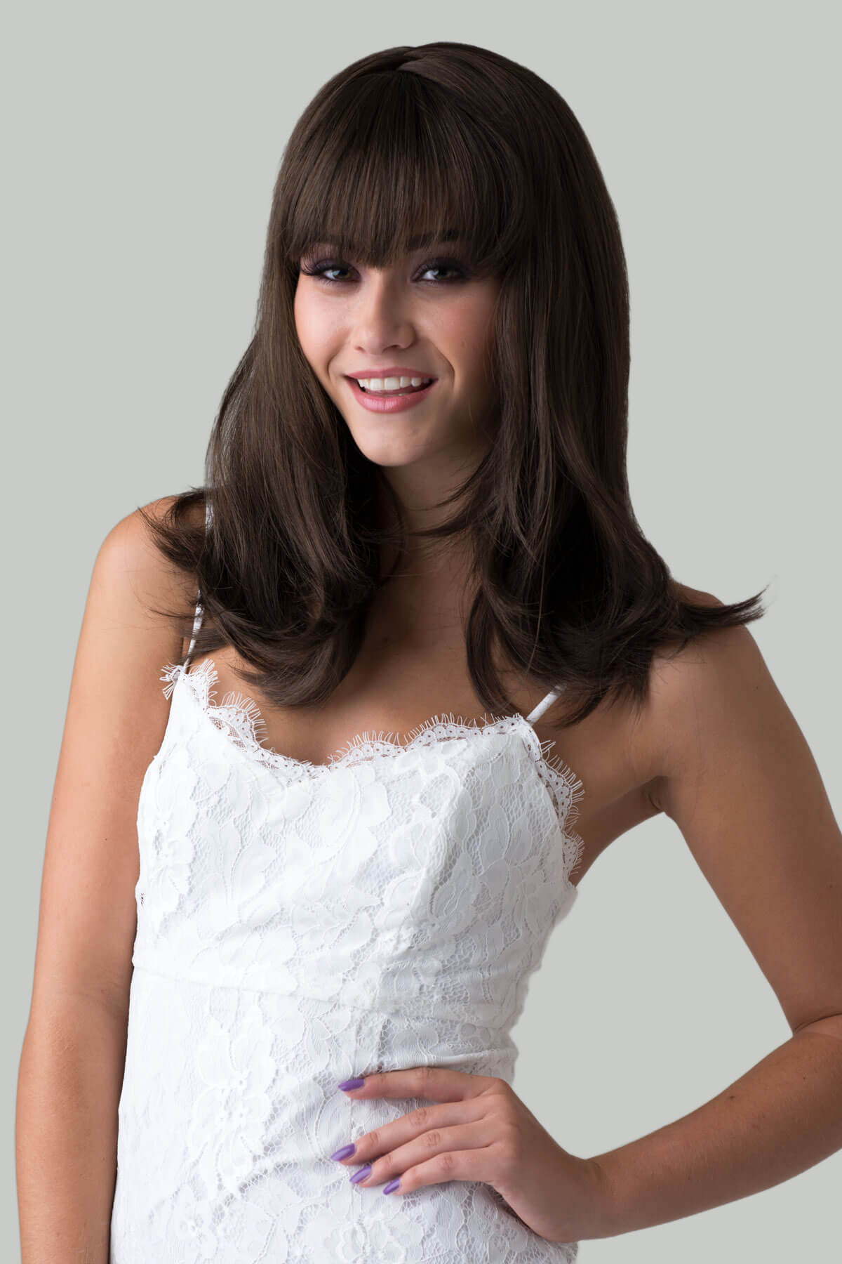 Woman wearing a white lace dress with a plain background. Brown long bob wig, layered with straight fringe: Katia chestnut brown 8