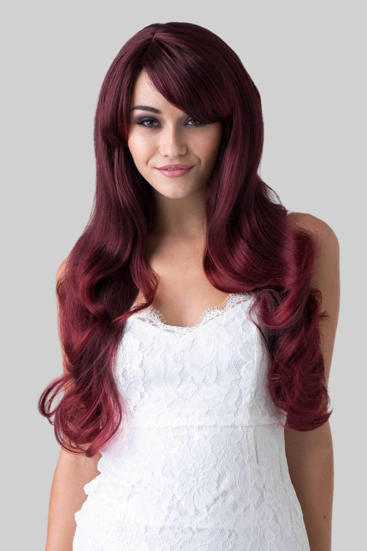 Woman with long burgundy wig wearing a white dress on a grey background. Long red wavy wig with black lowlights: Anji