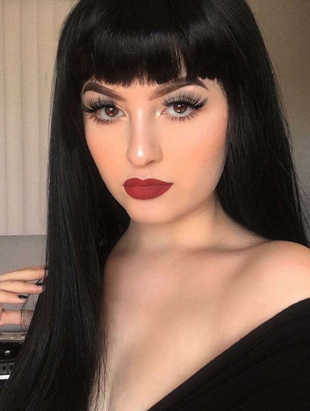 Woman with long black hair and red lipstick against a neutral background. Long straight black wig with straight fringe: Carmen