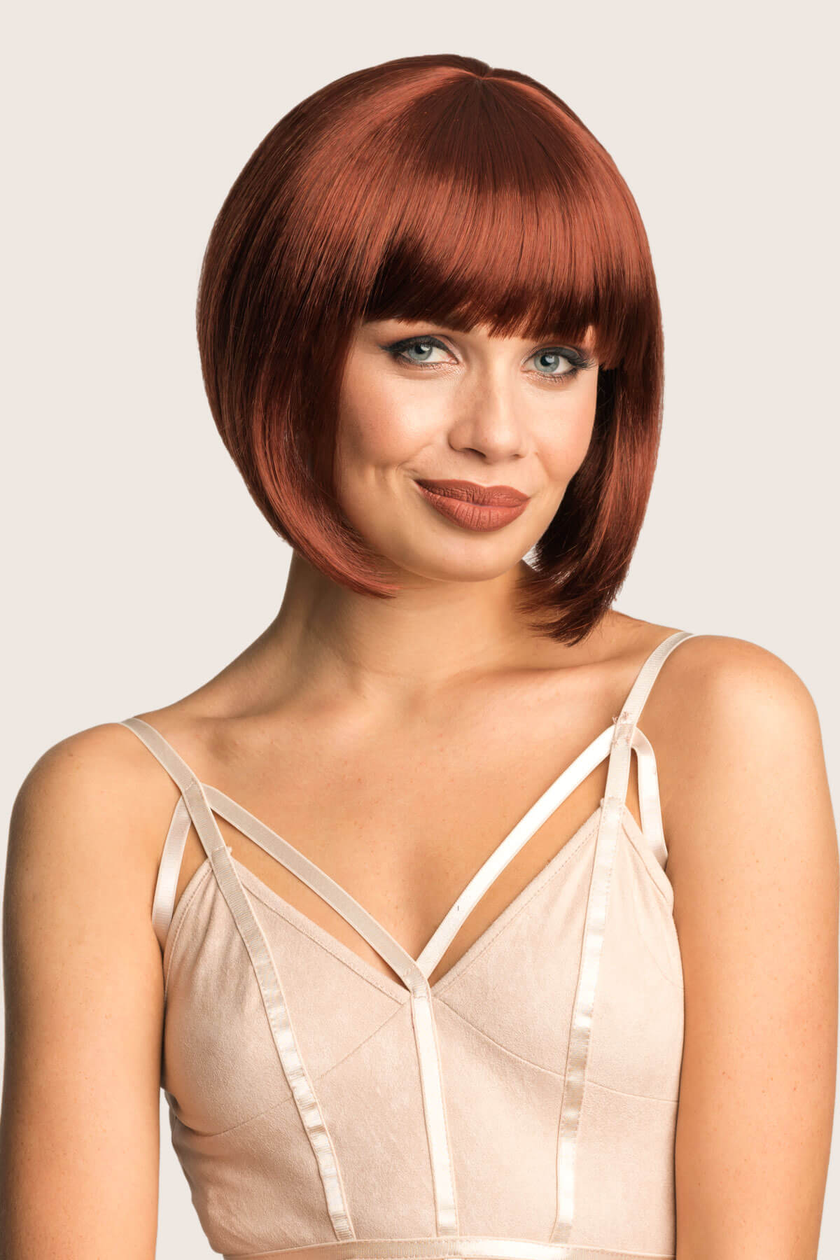 Woman with a stylish haircut wearing a beige dress against a plain background. Ginger/Copper red bob wig, Inverted / A-Line style: Jacqueline