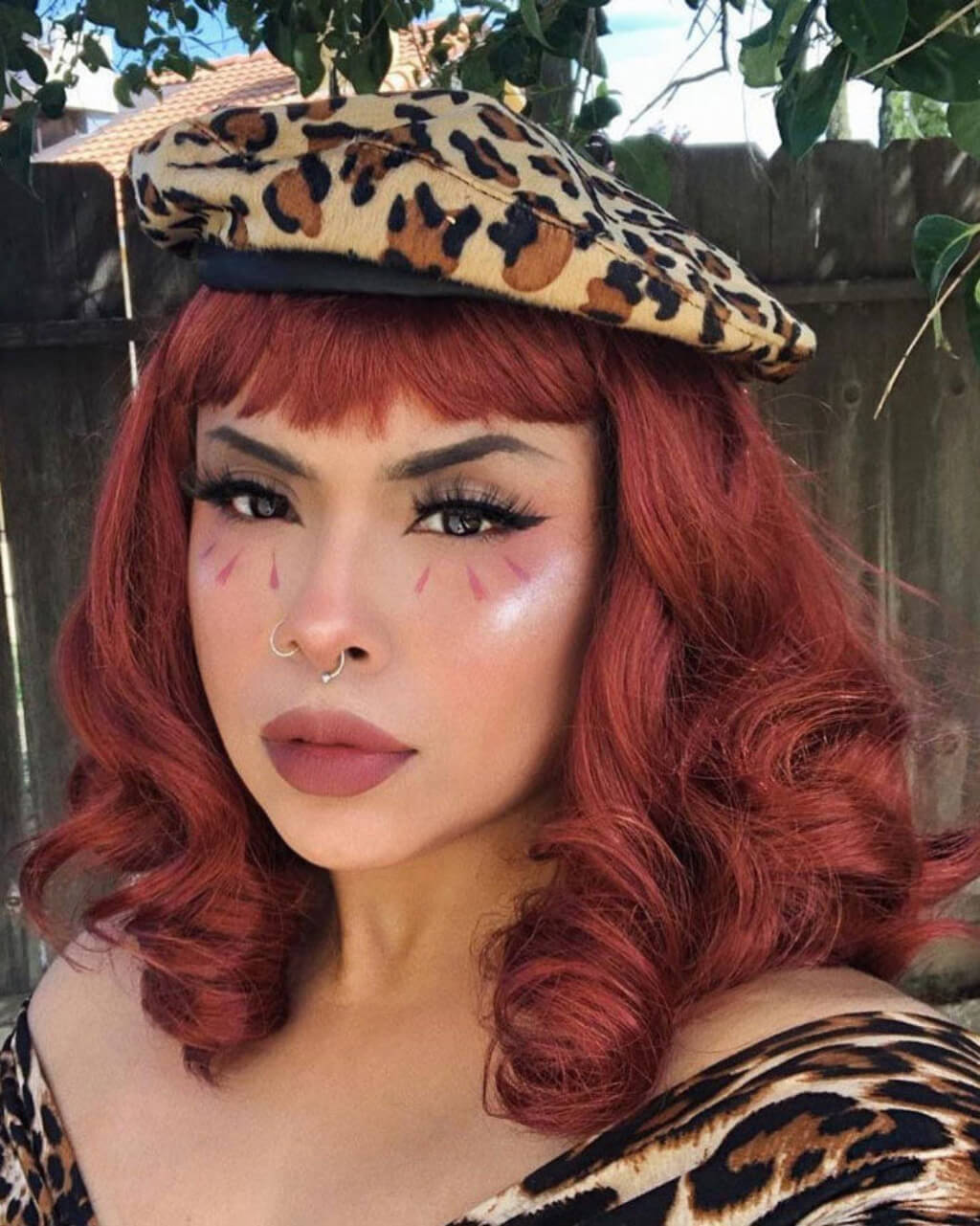 Person with red hair and leopard print beret outdoors. Copper red 1950s pinup wig, curled with short fringe: Kitty