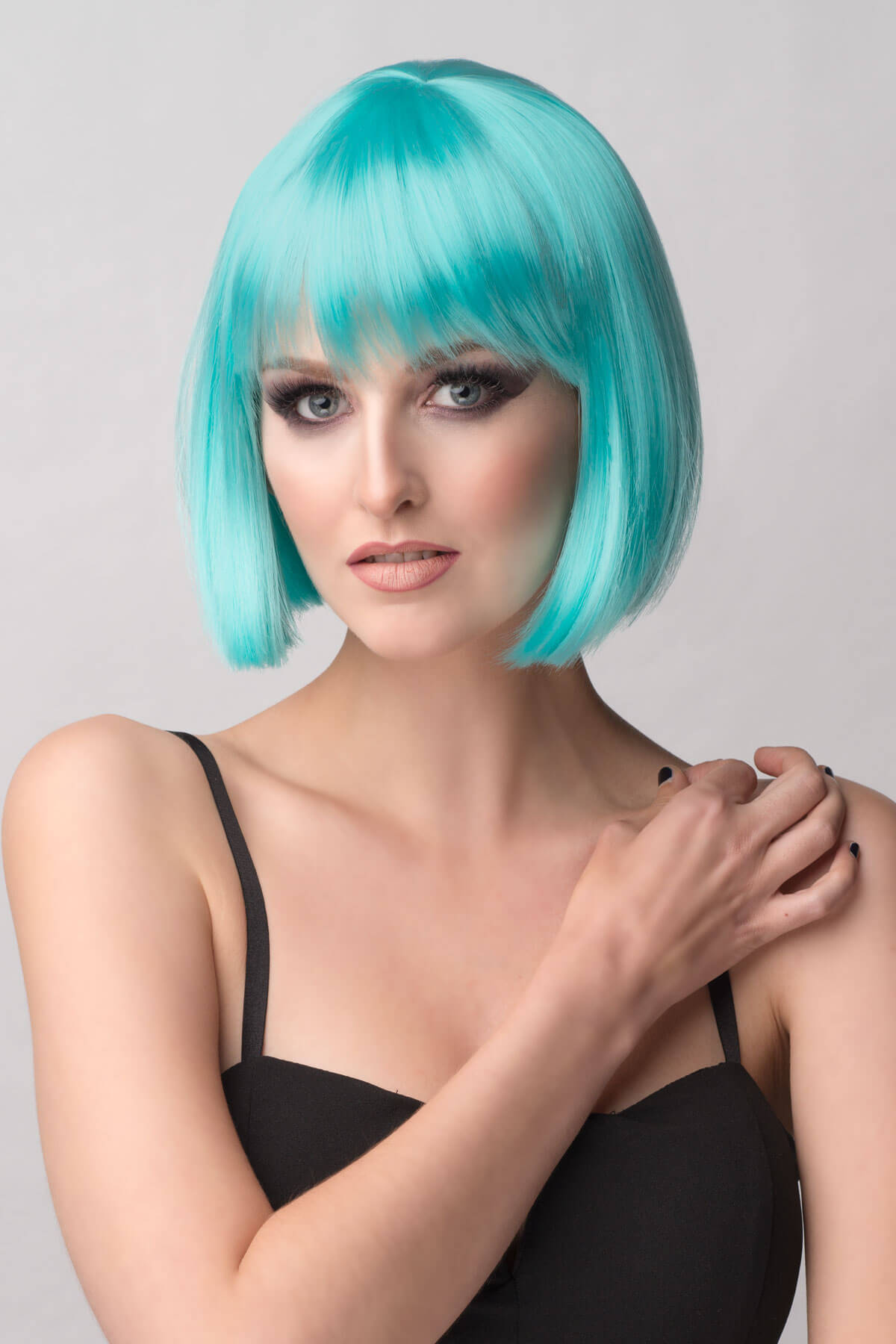 Woman with turquoise hair styled in a bob against a gray background. Turquoise bob wig  with full fringe: Iris